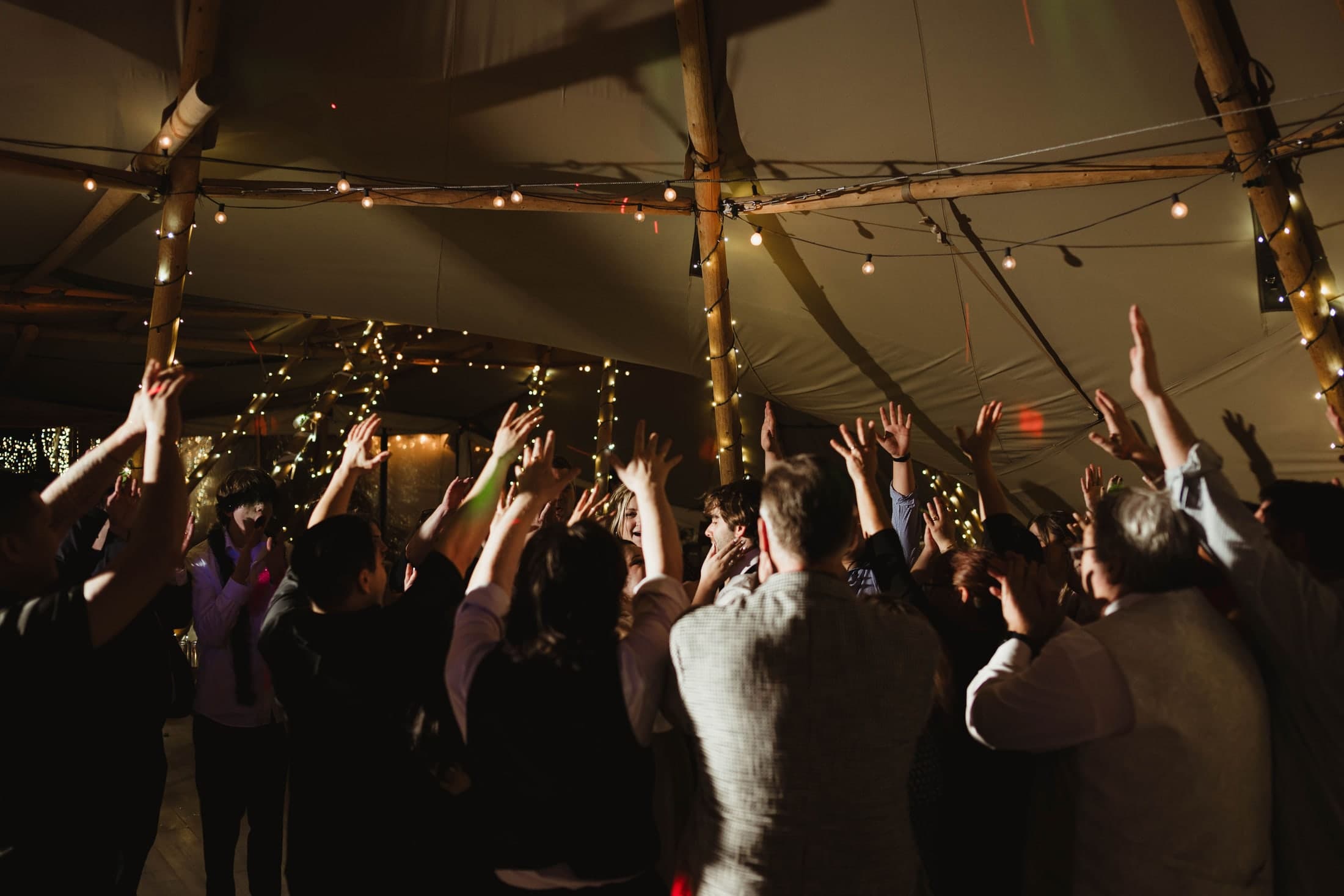 Wedding guests celebrating beneath string lights at Ben and Katie’s reception