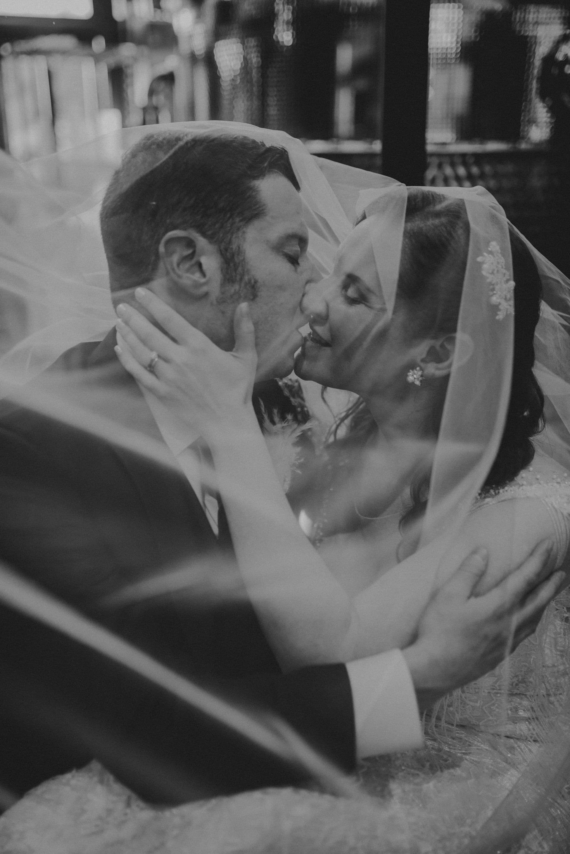 Chris and Amy sharing a kiss beneath her veil, photographed in black and white