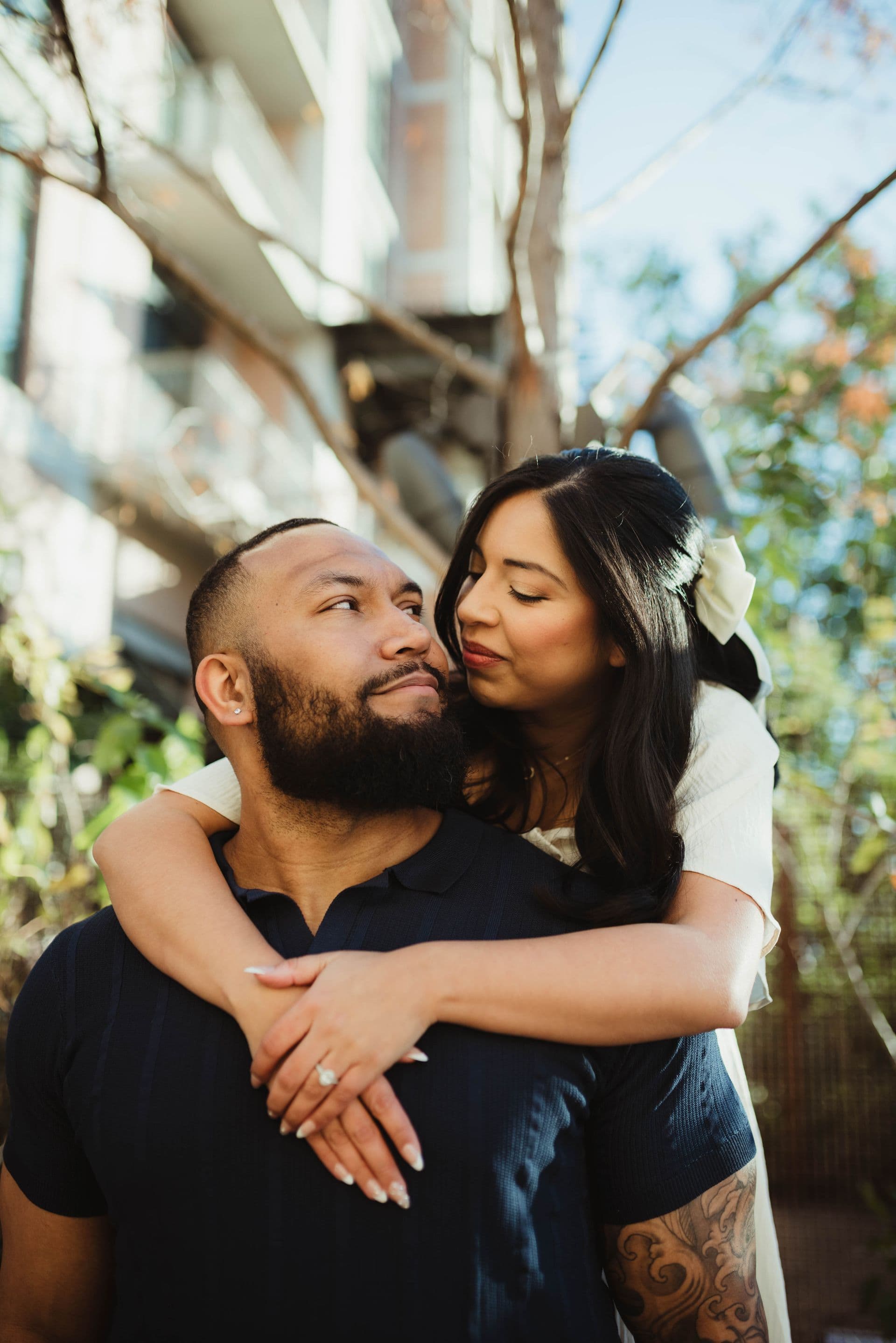 A couple holding each other close beneath leafy tree branches