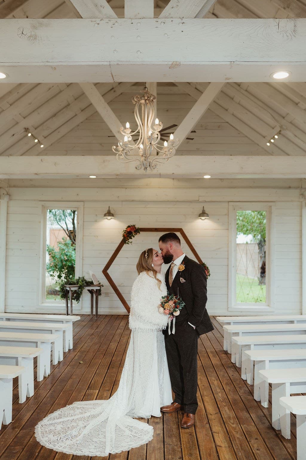 Brandon and Julia together in the aisle of a white chapel beneath a chandelier